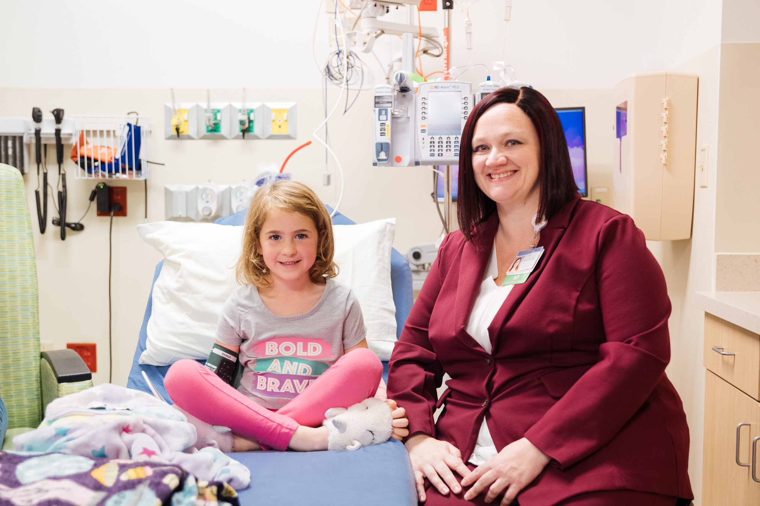 young girl with blonde sitting on patient bed next to pediatric gastroenterologist