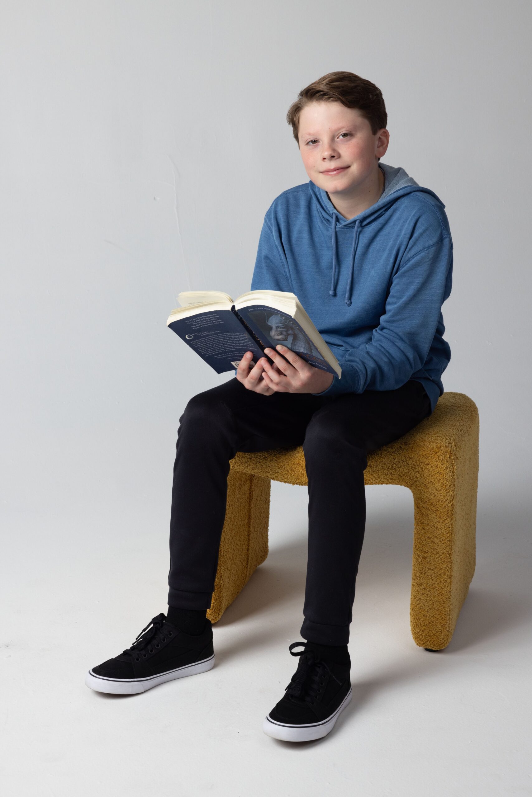 Teen boy in a blue hoodie sitting on a chair and reading a book, promoting children’s mental wellness and learning support.