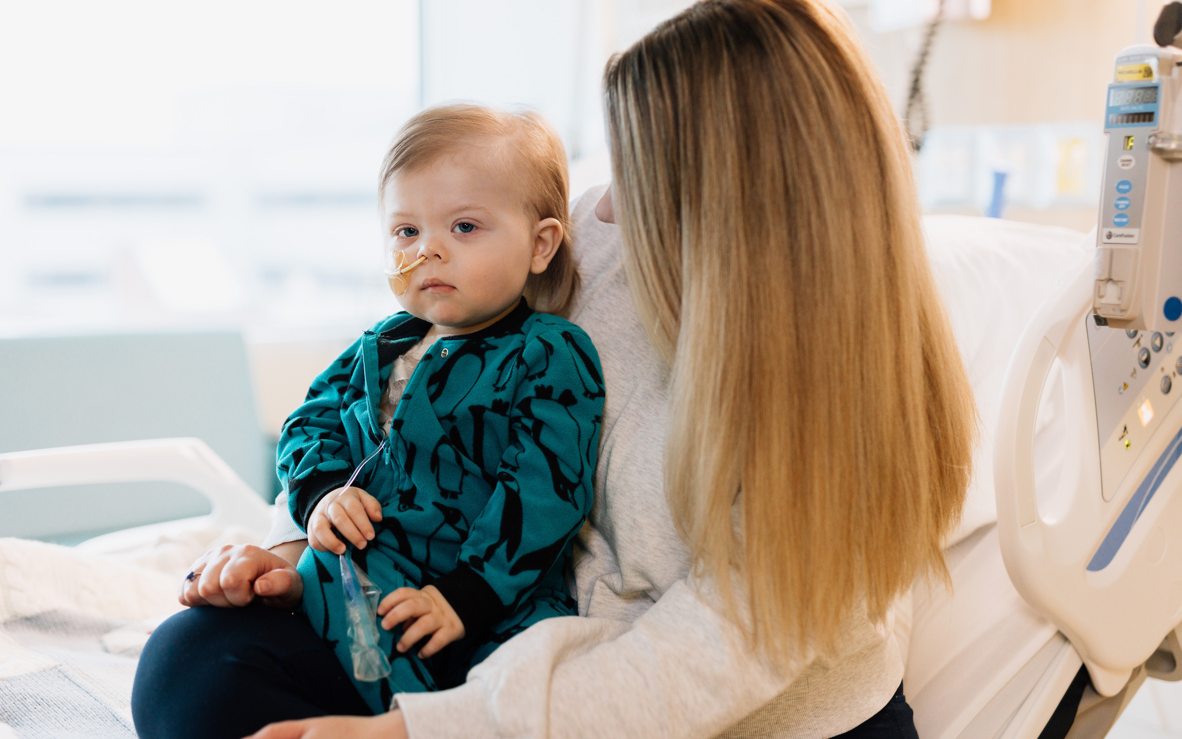 Young child held by mom in hospital while receiving treatment for cancer.