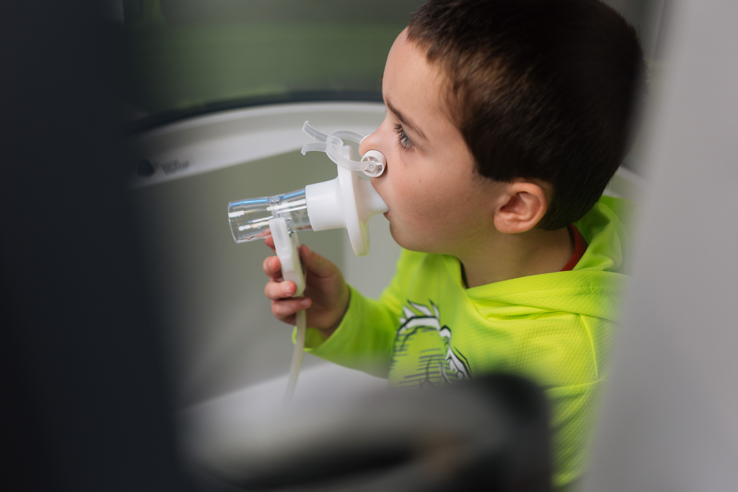 A young boy in a neon green hoodie using a nebulizer mask to inhale medication