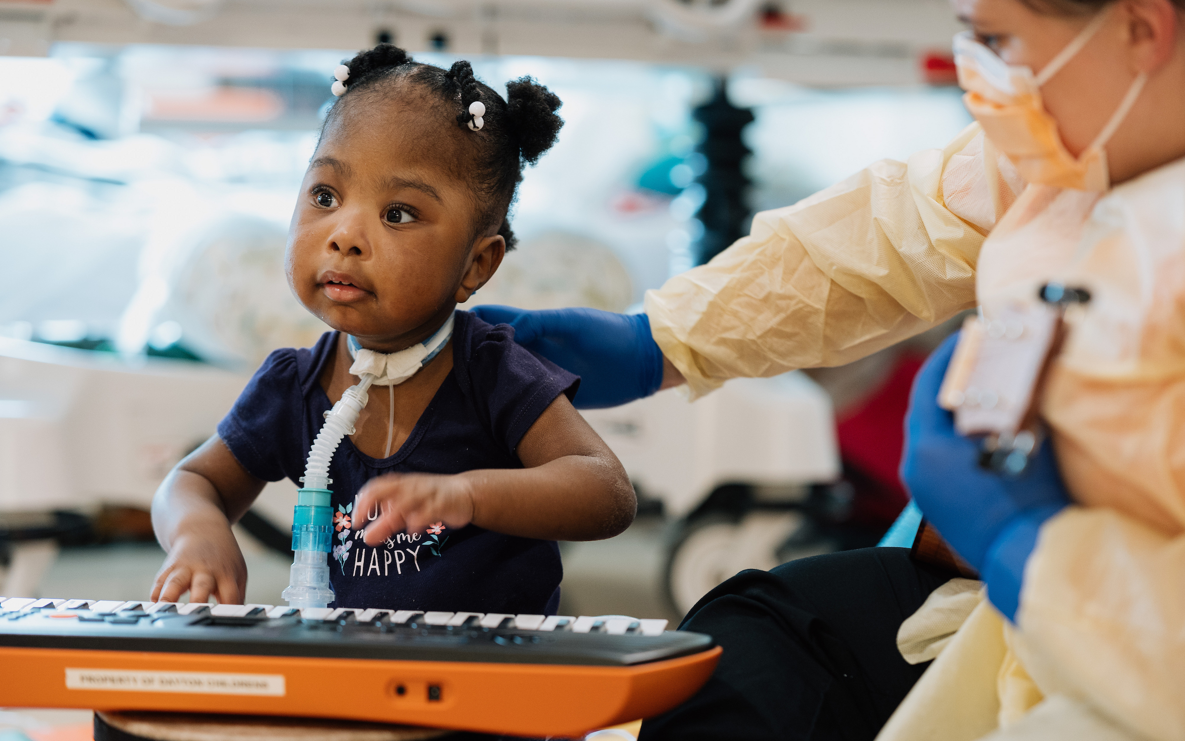 Young child with tracheostomy playing a toy keyboard with a care team member at Dayton Children’s Hospital.

