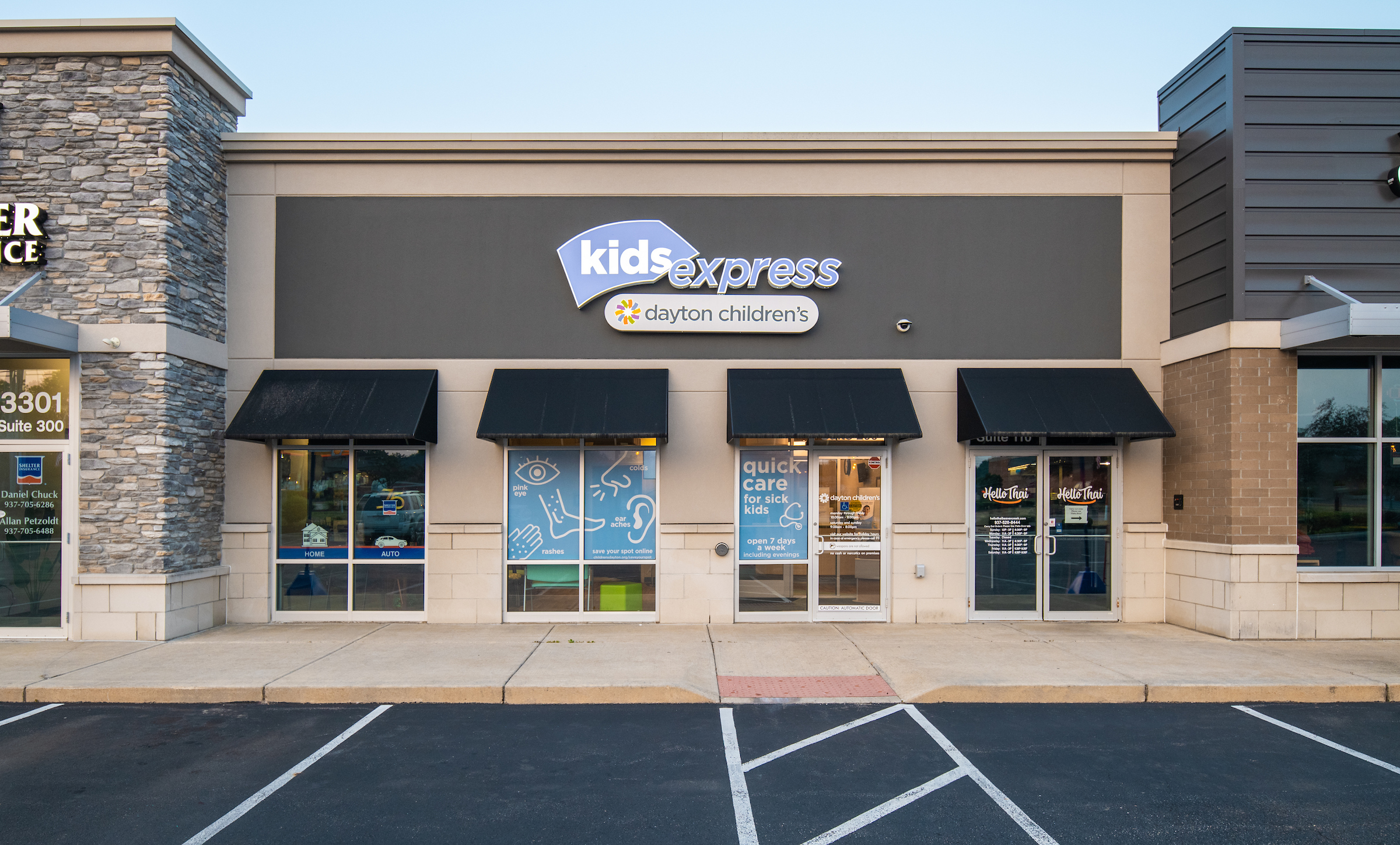The storefront of 'Kids Express by Dayton Children's,' an urgent care clinic with blue window signage advertising 'quick care for sick kids.' It is located between a 'NOW! DENTAL' office and a 'VIVI Bubble Tea' shop in a strip mall.