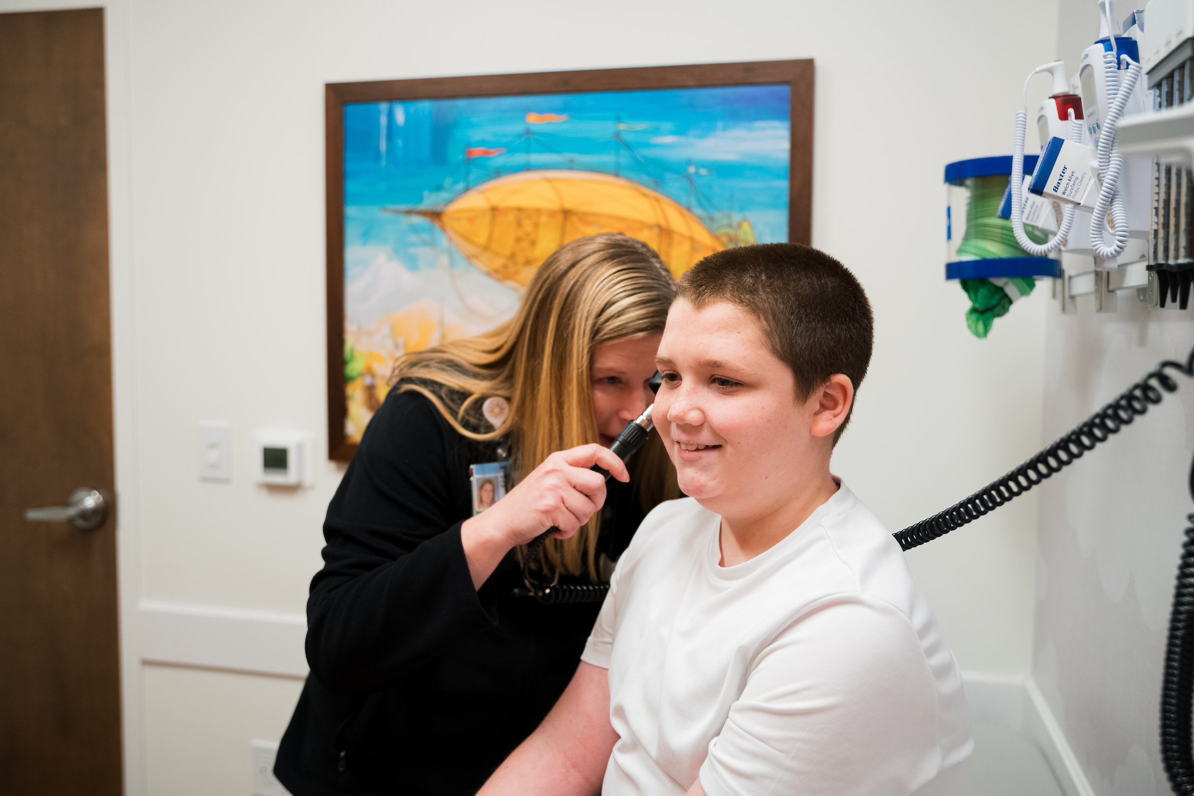 A medical professional examining a smiling young patient's ear with an otoscope.