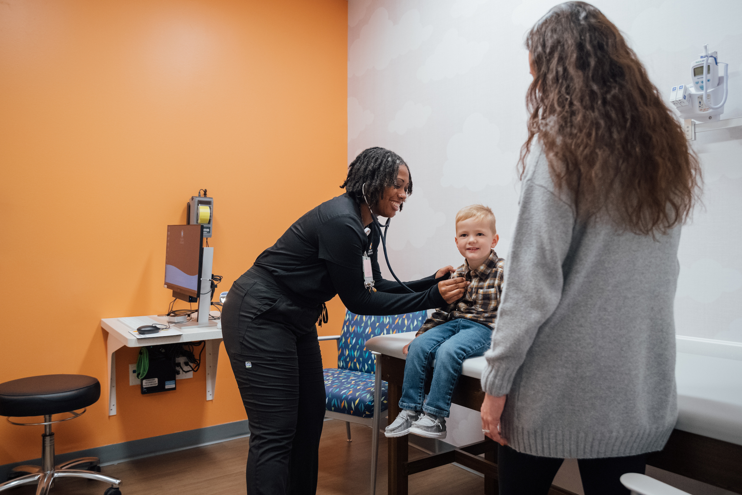 Friendly pediatric nurse practitioner with child and parent in a Kids Express clinic for a minor illness.