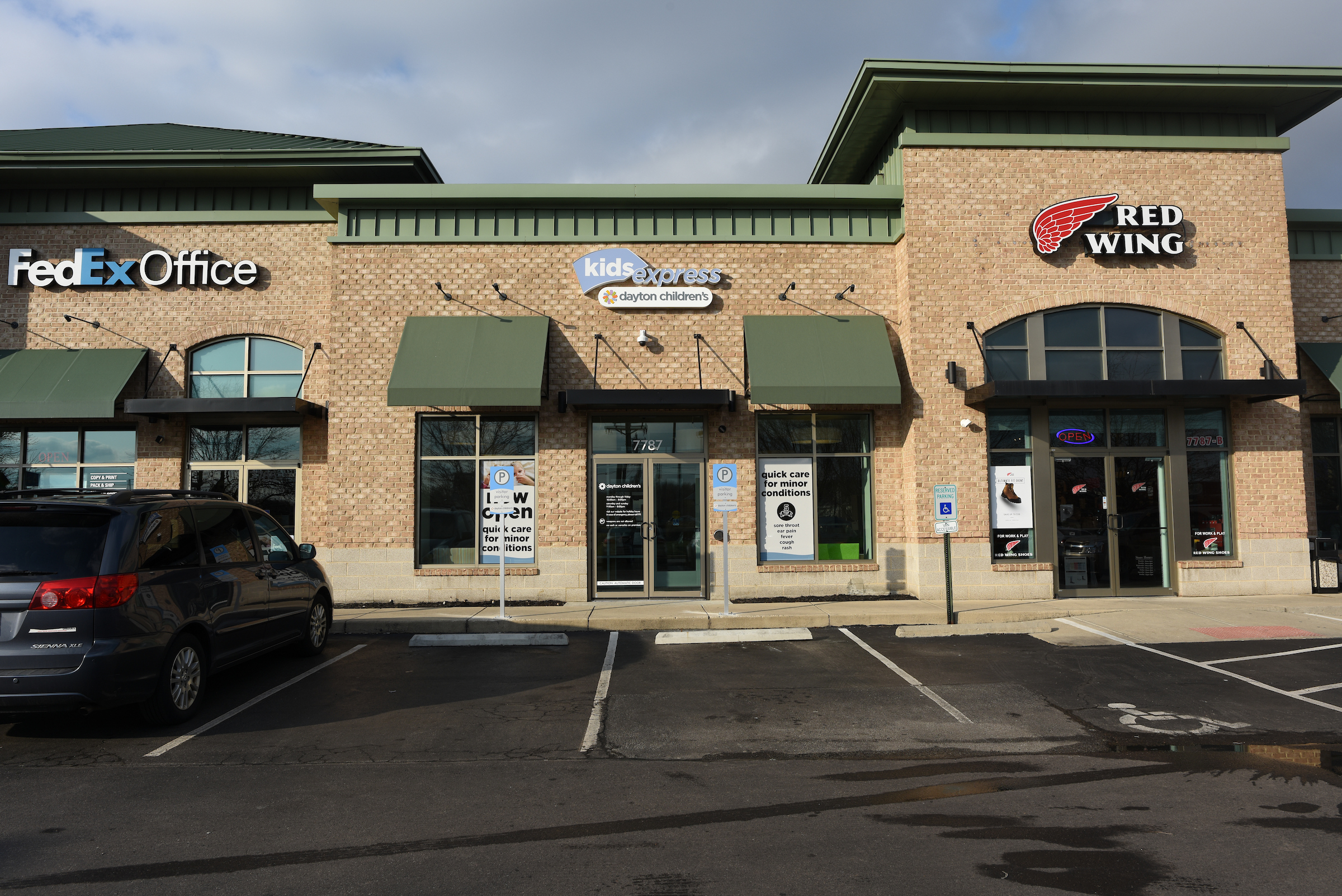 A street-level shot shows a modern, brick strip mall with three businesses: FedEx Office, Kids Express, and Red Wing.