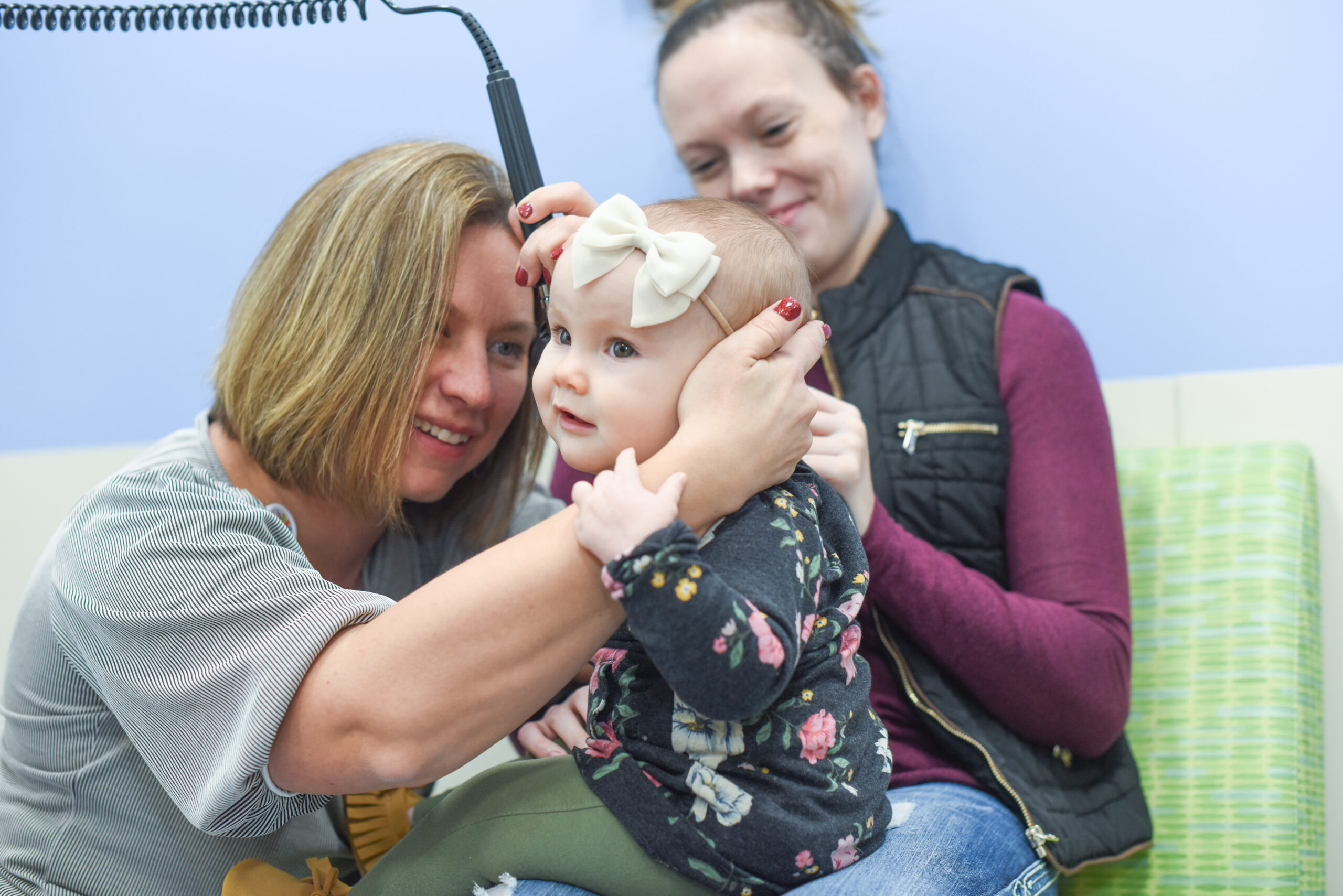 A doctor examining a baby's ear, with another woman smiling in the background.