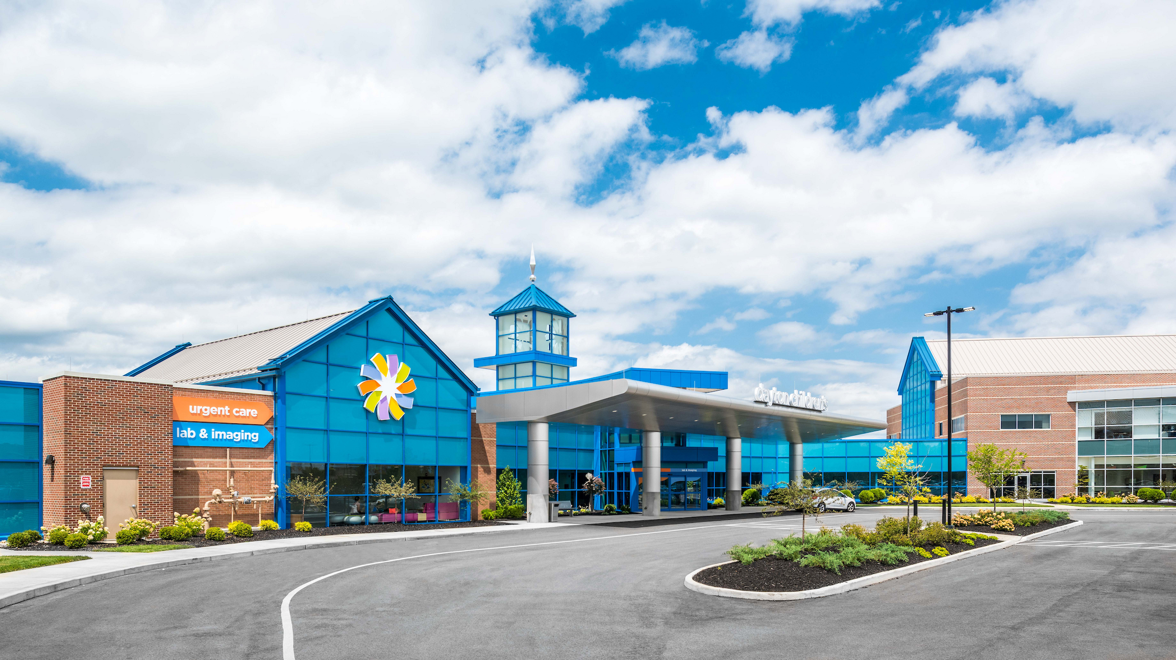 Exterior of a colorful children's hospital with blue facade, brick accents, and 'Urgent Care' signage under a cloudy sky.

