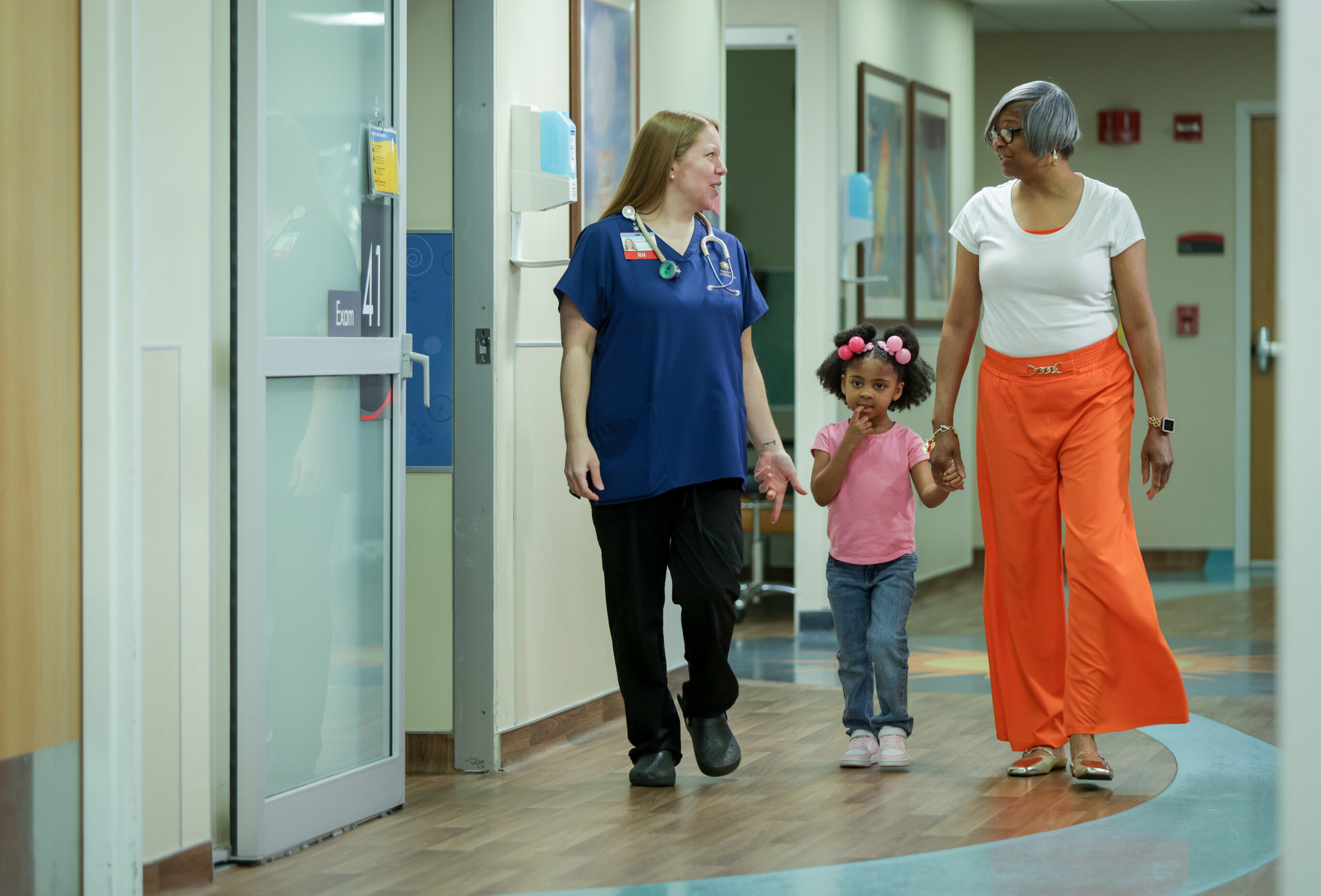 A healthcare provider accompanying a young patient and their guardian through a hospital