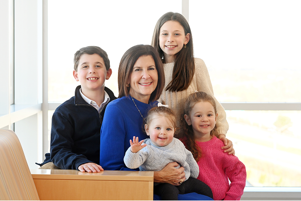 A smiling adult with children poses together in a bright space, representing hospital leadership and the community-focused mission behind pediatric care.