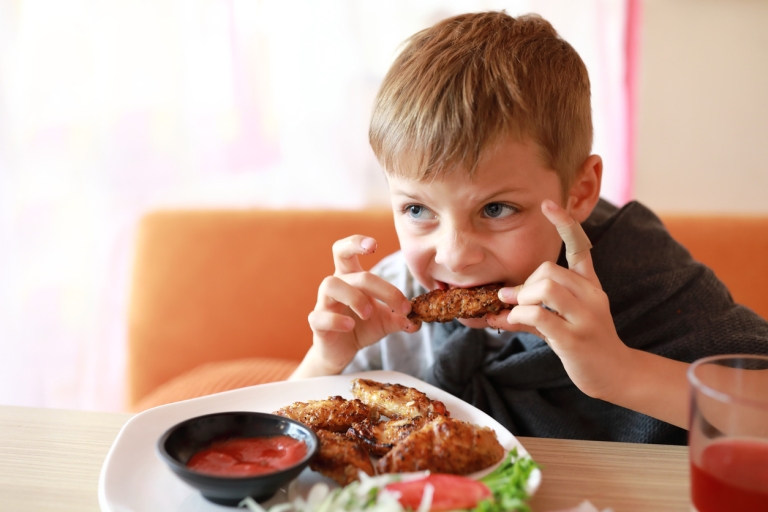 Young boy eating fried chicken wings, a common cause of indigestion in kids