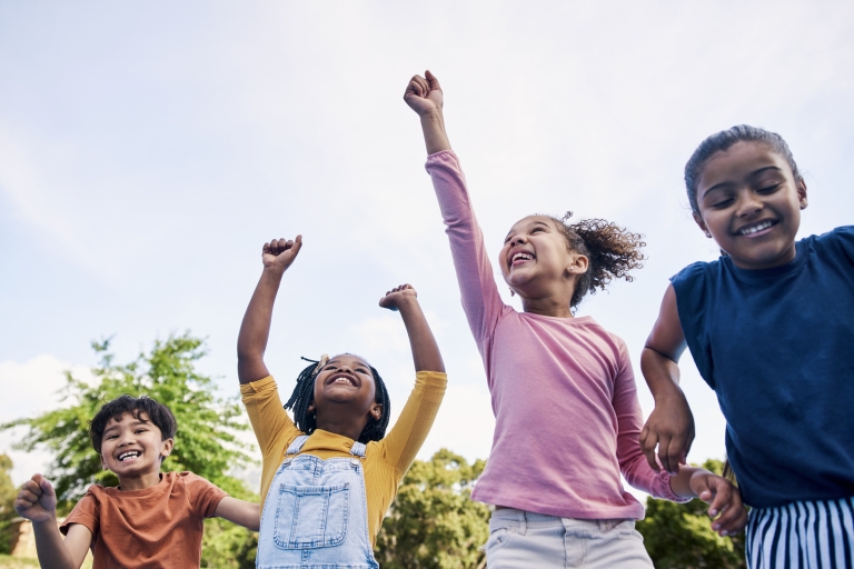 Group of four energetic kids jumping with hands in air