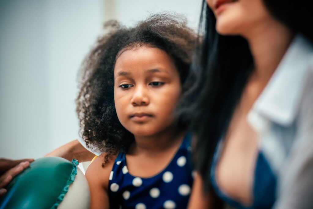 Girl sitting next to caretaker looking uncomfortable with physical discomfort.