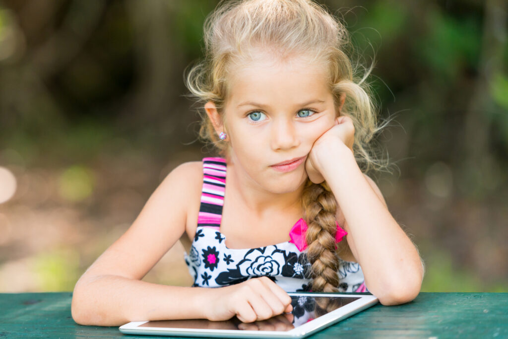 little girl sitting outside with iPad with symptoms of absence seizures