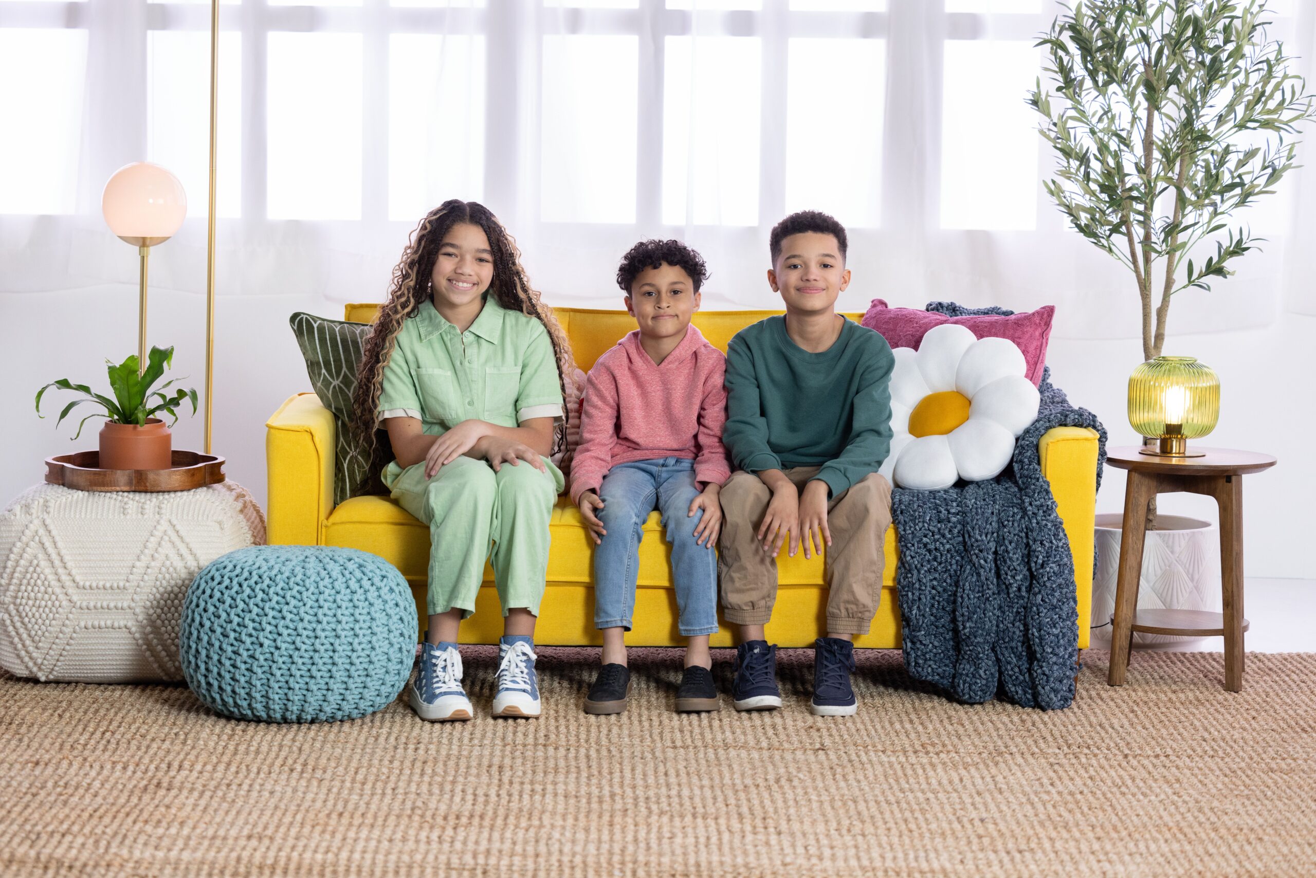 Three smiling kids sitting on a bright yellow couch with colorful pillows, symbolizing children’s mental health support.