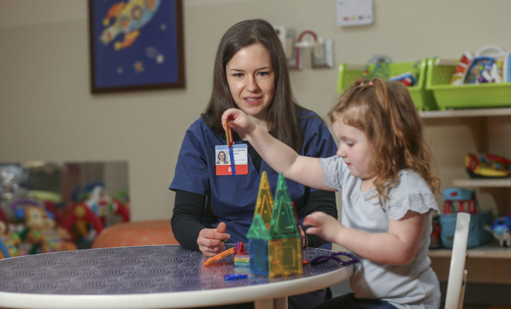 A Dayton Children’s psychiatry nurse plays alongside with  young girl building a house with magnetic tiles.

