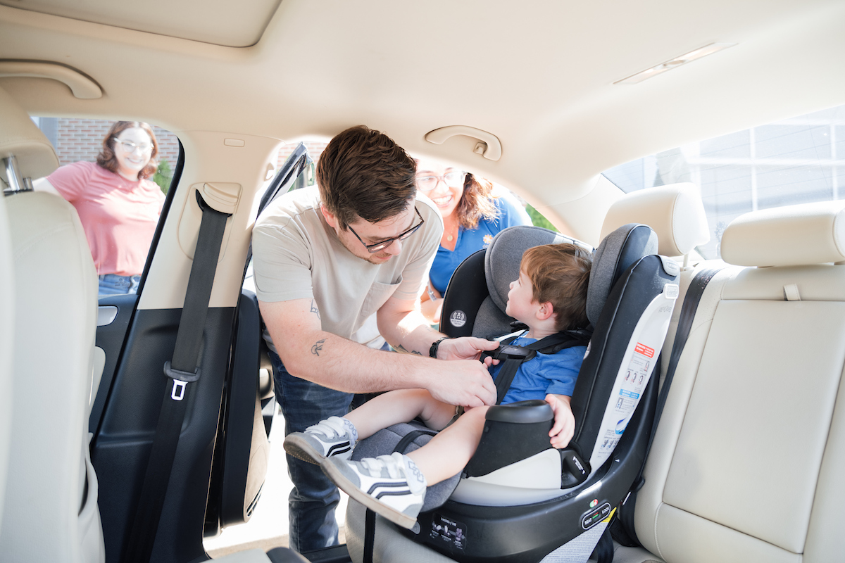 Smiling toddler sitting safely in a car seat inside a vehicle, looking happy and comfortable.