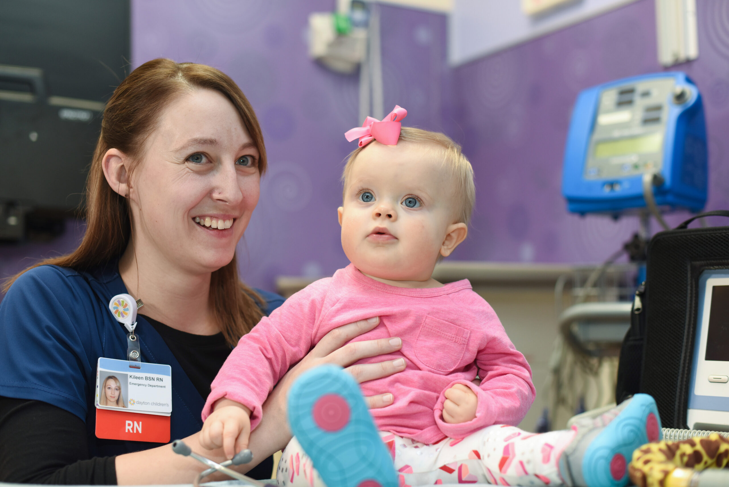 A Dayton Children’s nurse holds a cute baby girl wearing a matching pink bow and shirt.


