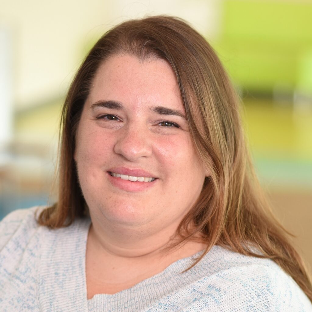 A smiling woman with auburn long hair wearing a white sweater.