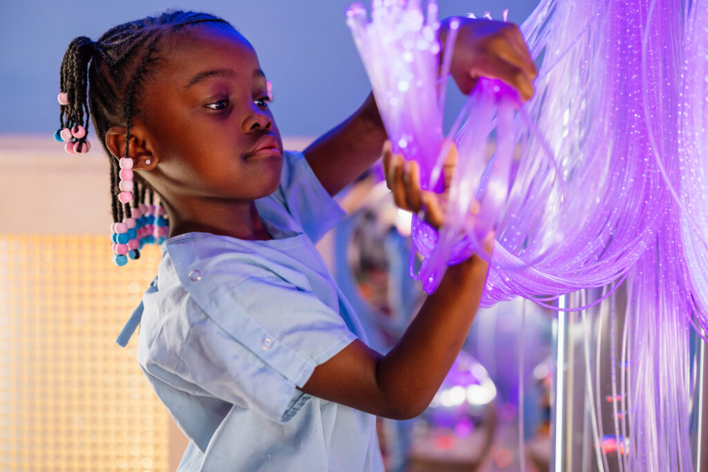 Young girl calmly plays with sensory friendly lights as she is preparing for surgery in pre-op room.