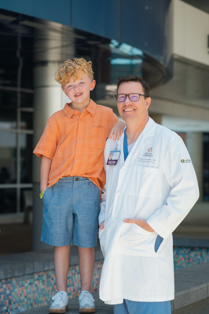Dr. Lober, lead of the biobank, stands smiling with a young boy outside the hospital.