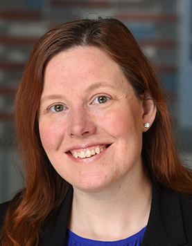 Close-up headshot of a smiling woman with long reddish-brown hair and small stud earrings