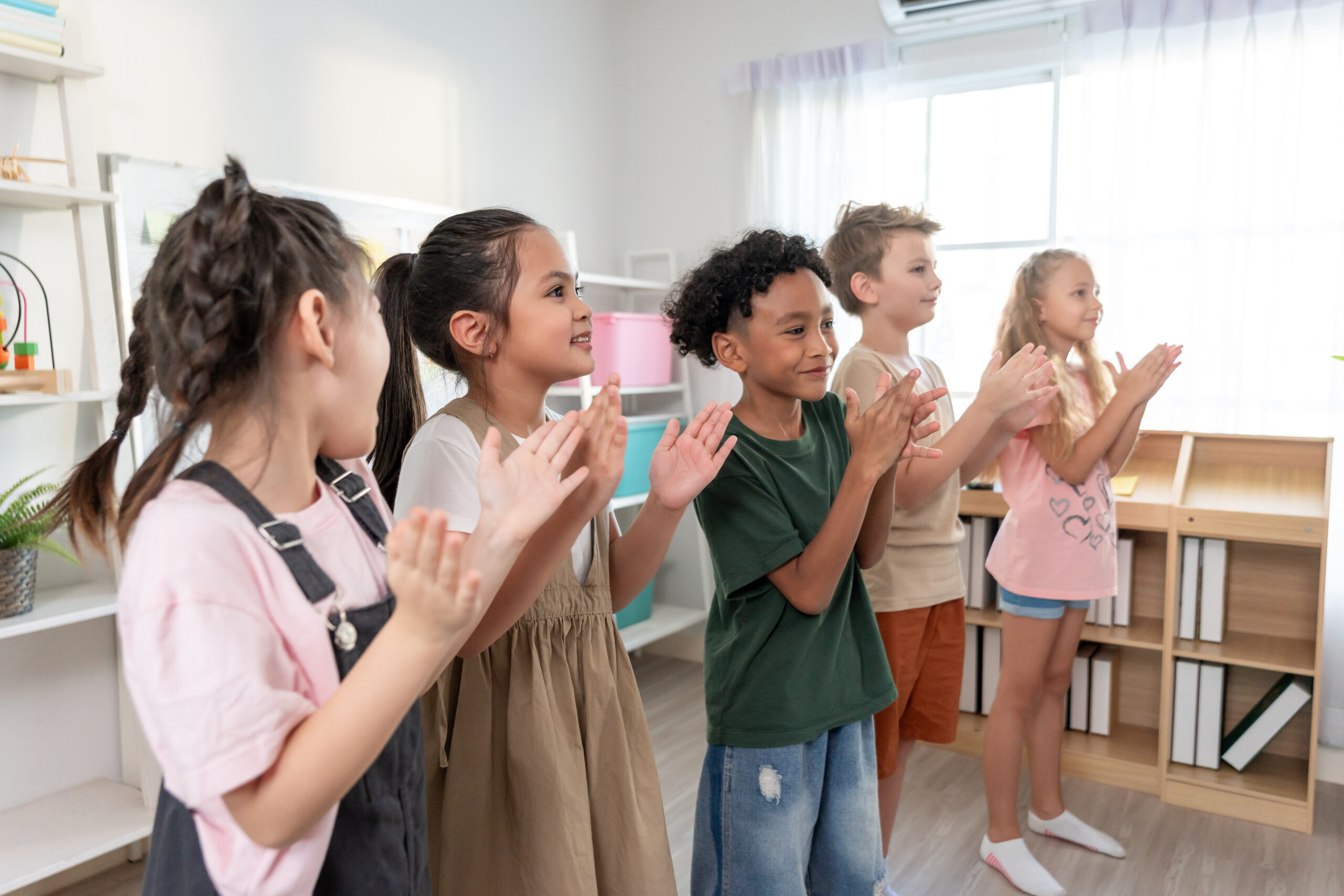 Group of adorable student clapping hands at nursery school. Adorable schoolboy and girl feel happy and enjoy back to school, learning with teacher in classroom at elementary kindergarten.