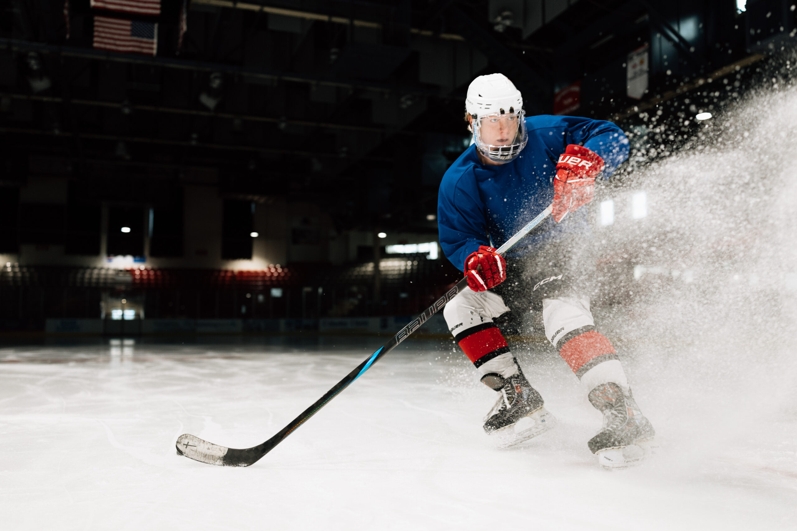 Teen ice hockey player holding hockey stick while training at ice rink.