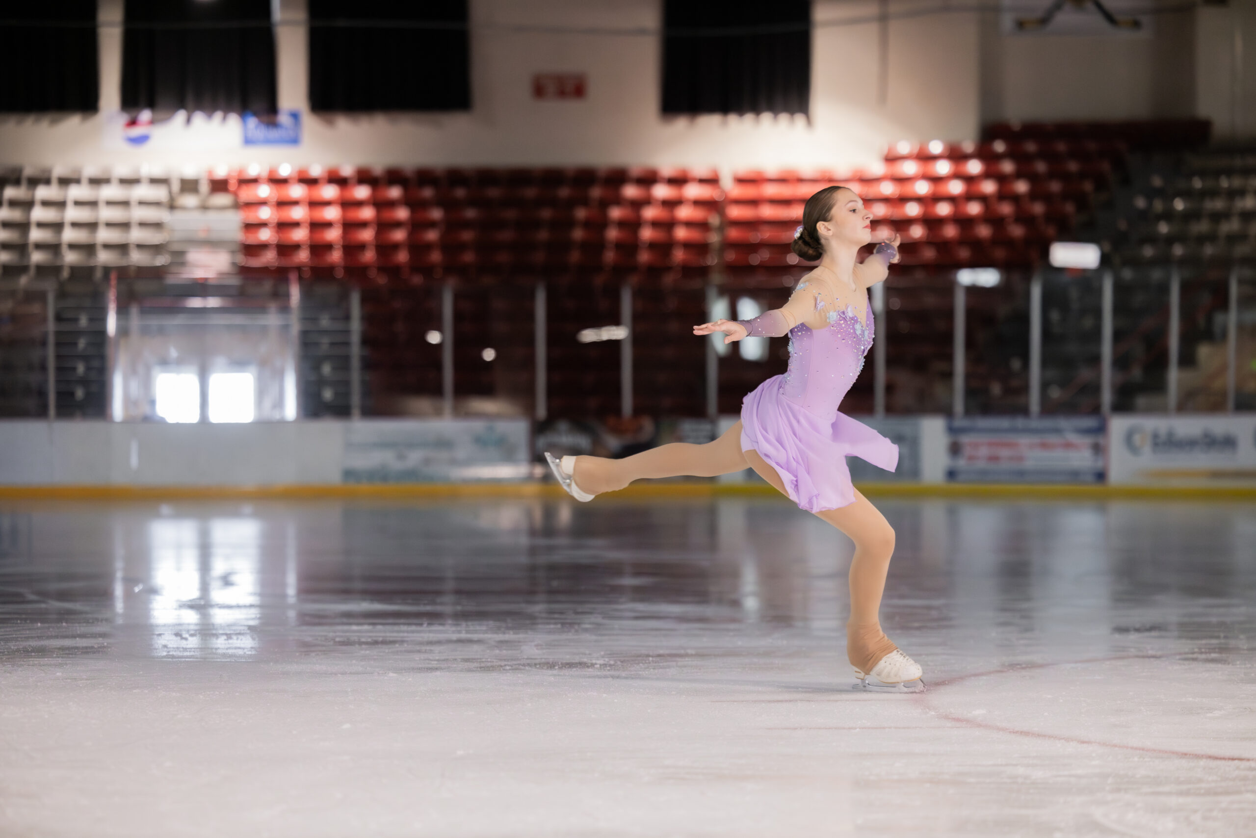 Focused, young female ice skater training on ice rink.