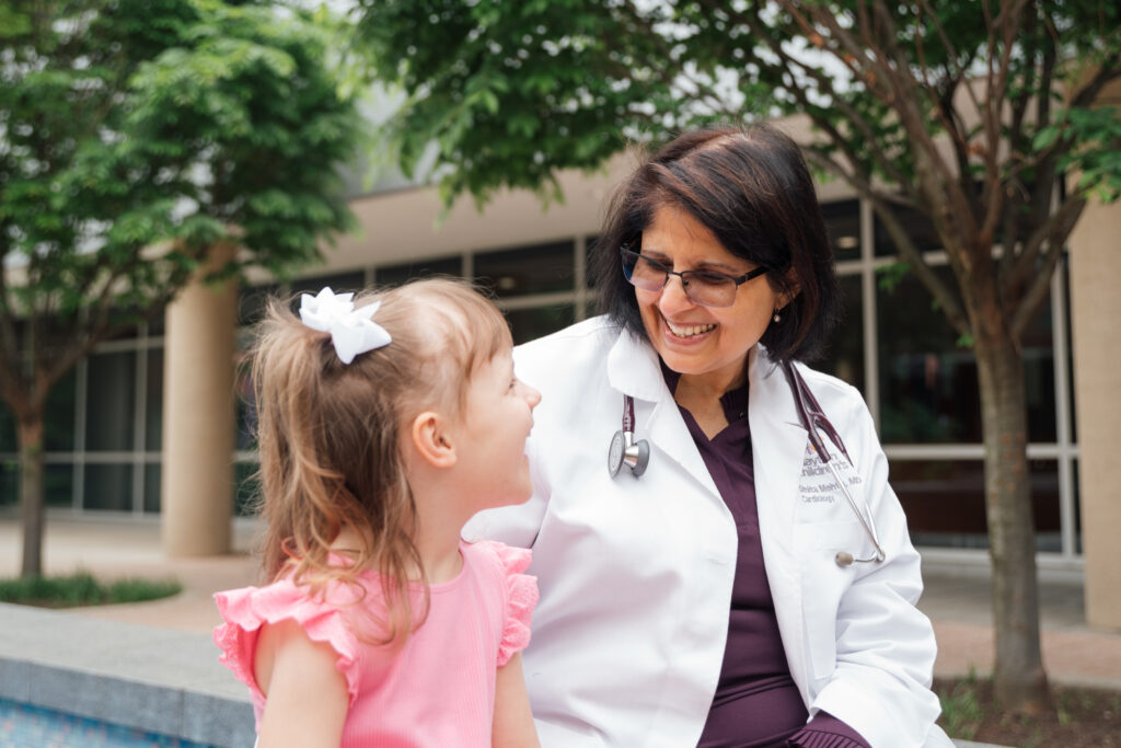 Pediatric cardiologist poses with patient and smiles