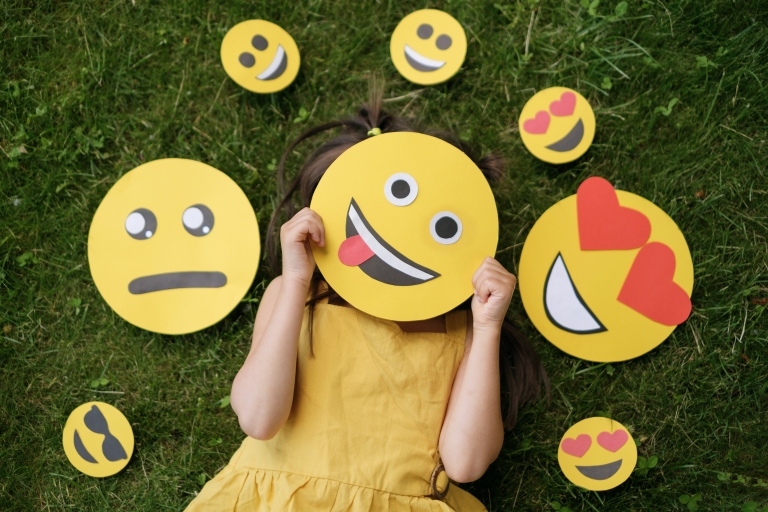 young girl plays with emoji masks of all kinds of emotions