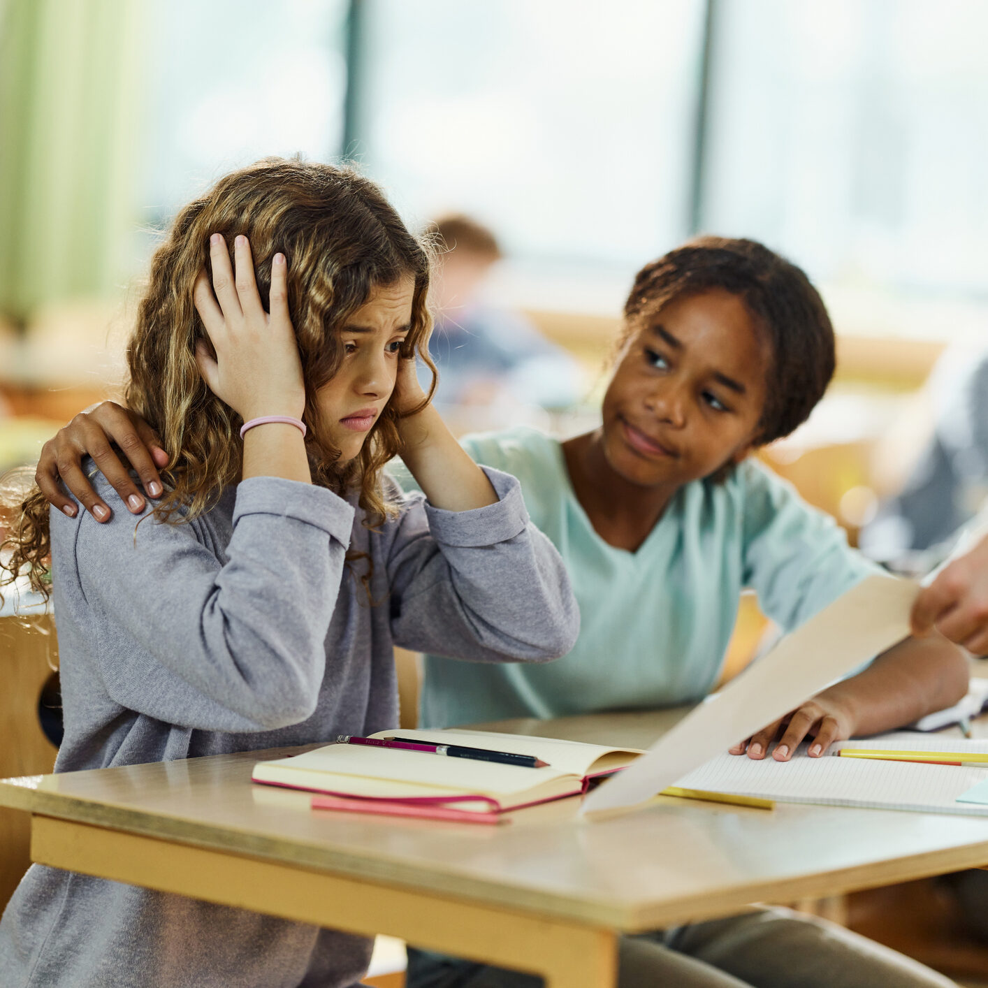 Young female student is upset in class and being consoled by her classmate