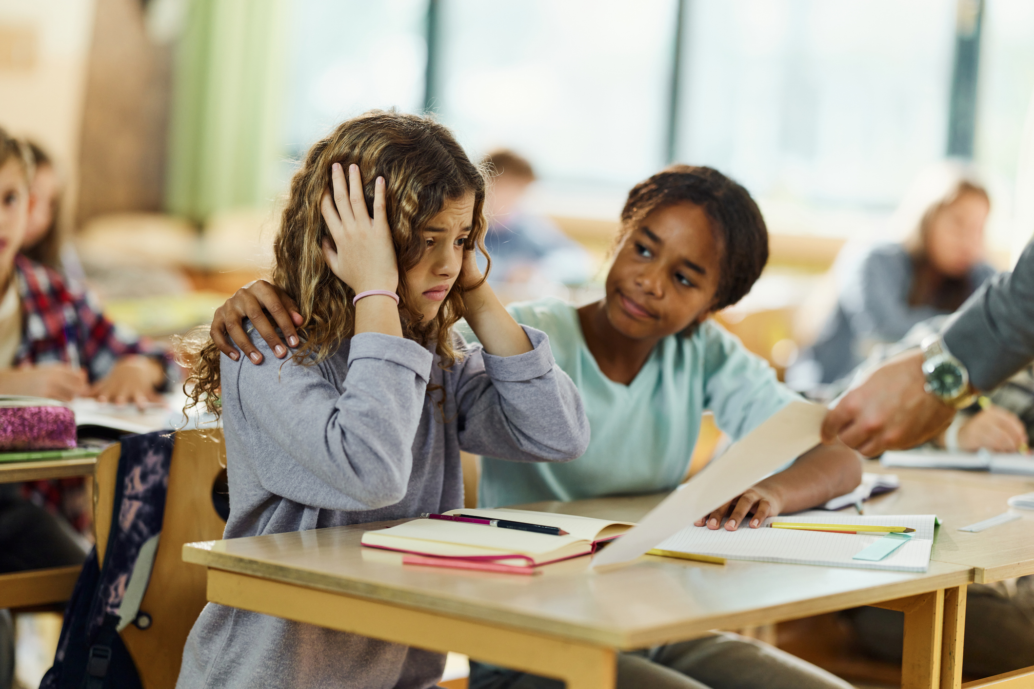 Young female student is upset in class and being consoled by her classmate