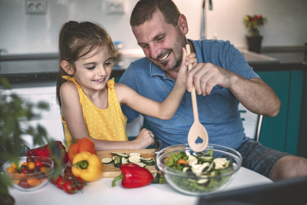 Father figure cooking healthy foods with young girl in kitchen