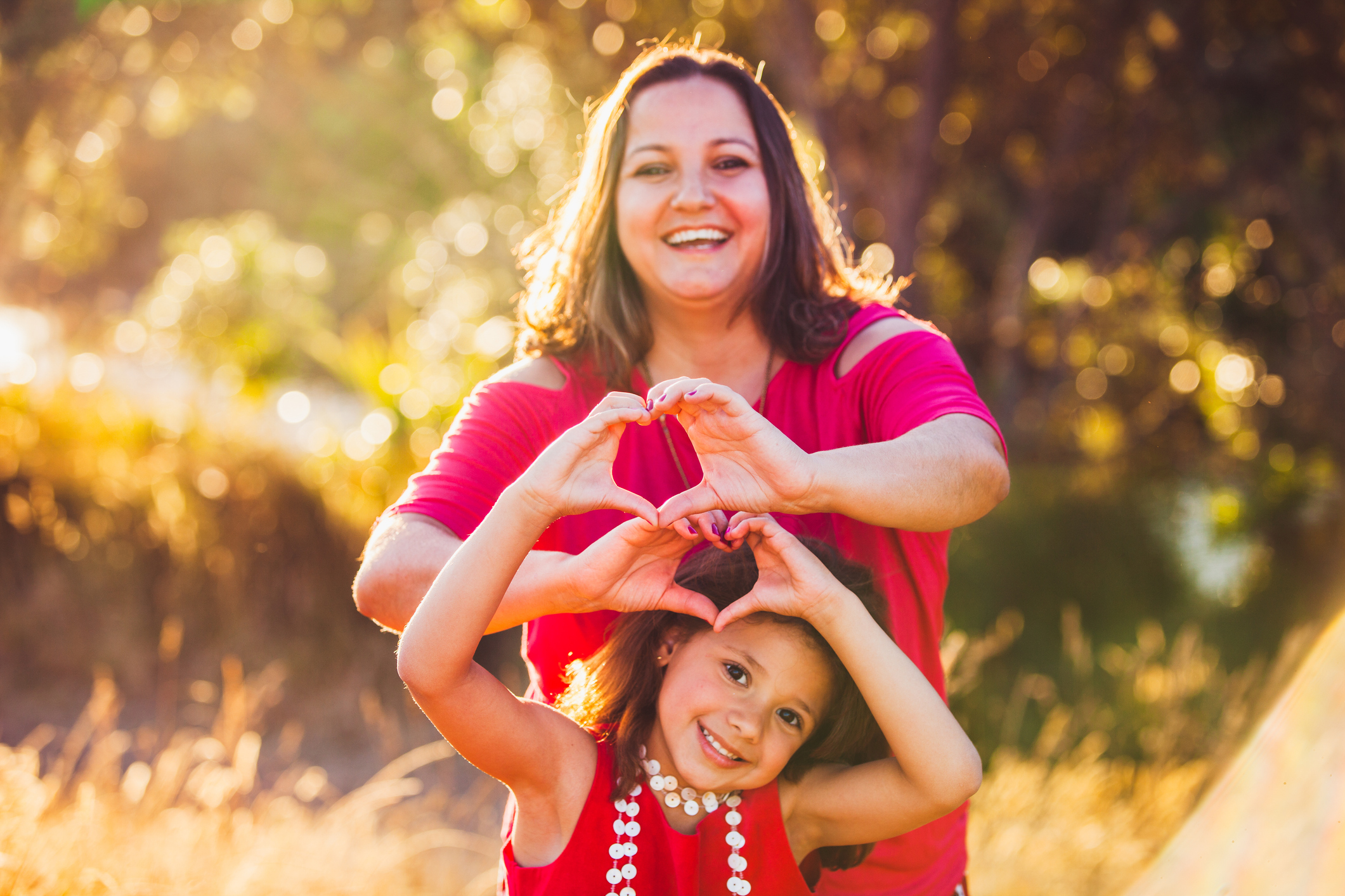 Mother figure makes heart hands with young girl in a park