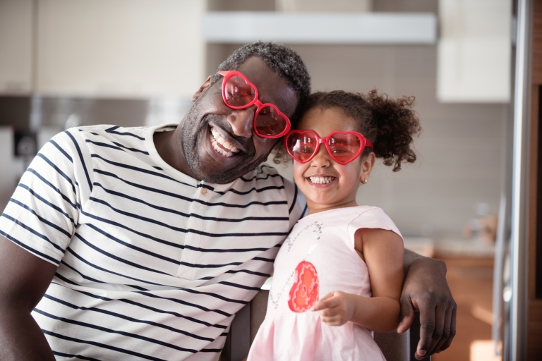 father and daughter smile playfully while wearing heart-shaped glasses