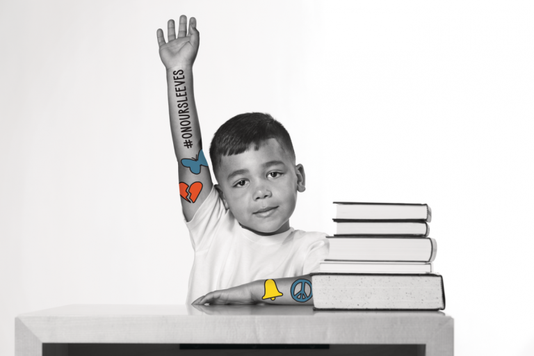 young boy raising hand at school desk