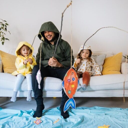 Father plays pretend fishing game with two young children at home