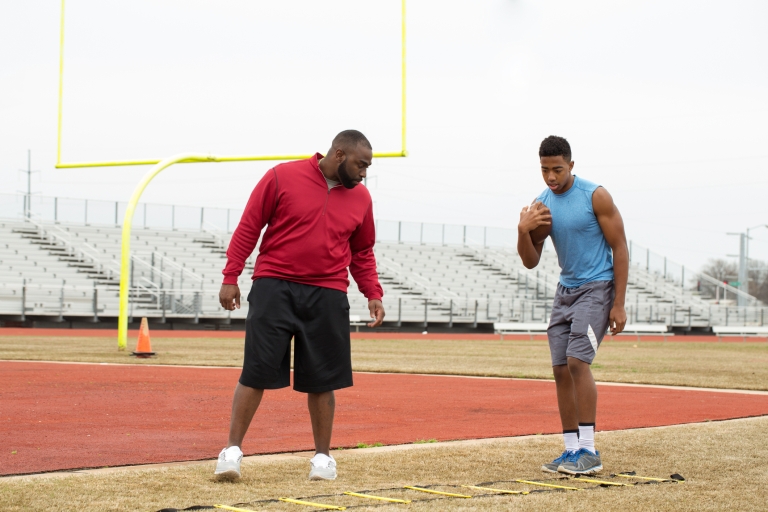 teen at football practice doing drills with a coach