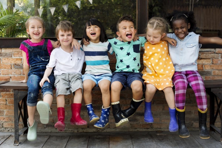 a group of children smile together while sitting on a bench