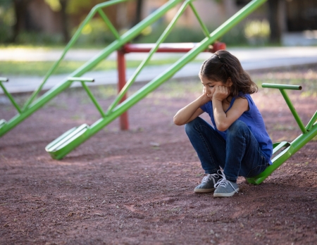 child sitting at a playground looking lonely