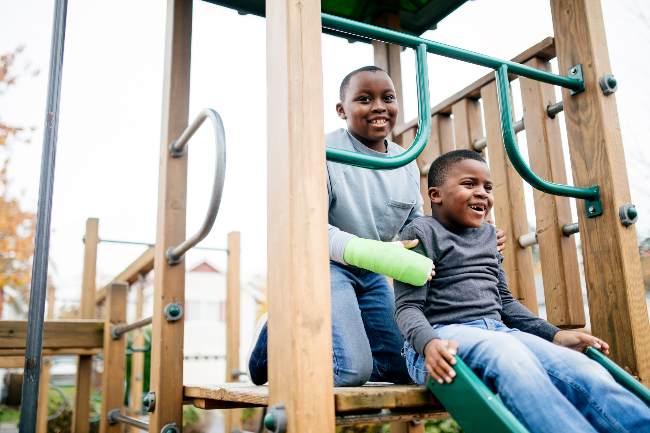 A young boy in a cast plays with his brother on the playground.
