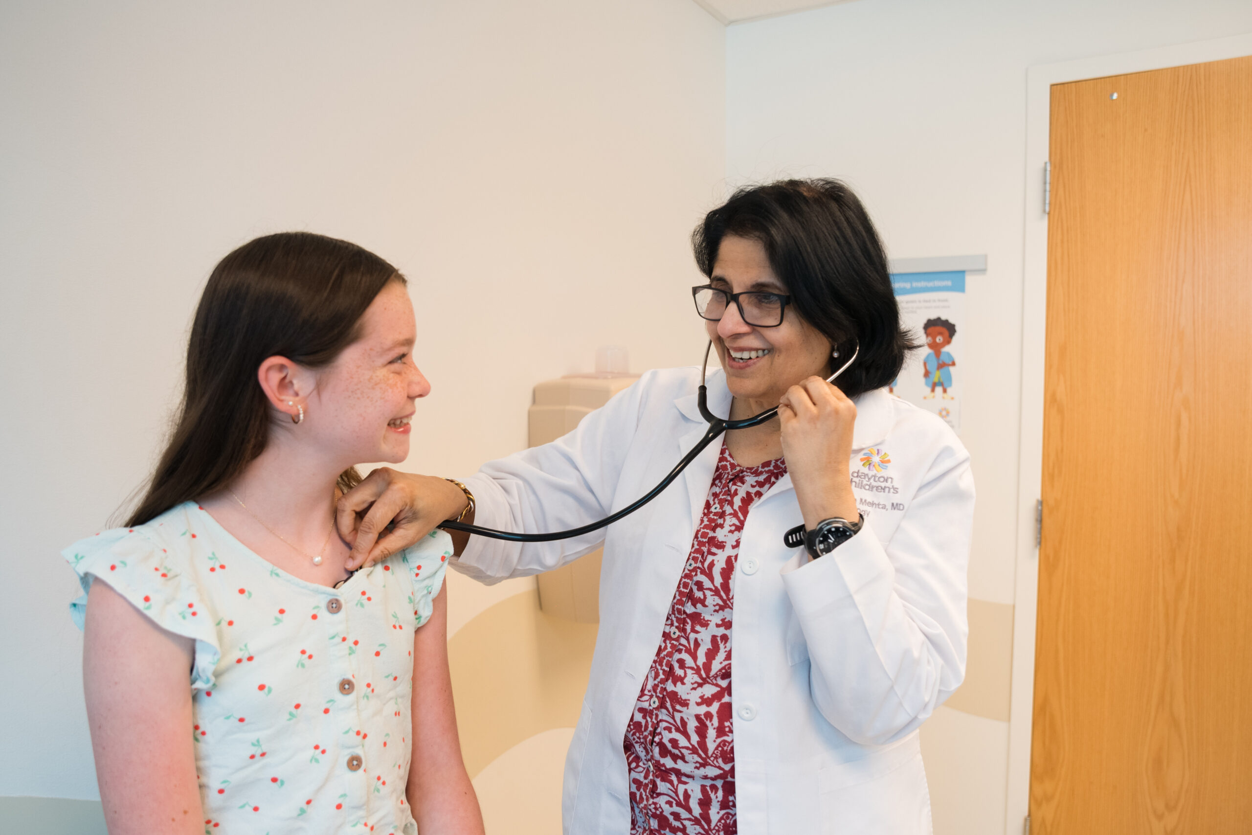 Female doctor smiling with preteen female patient while listening to her heart at a sports physical.