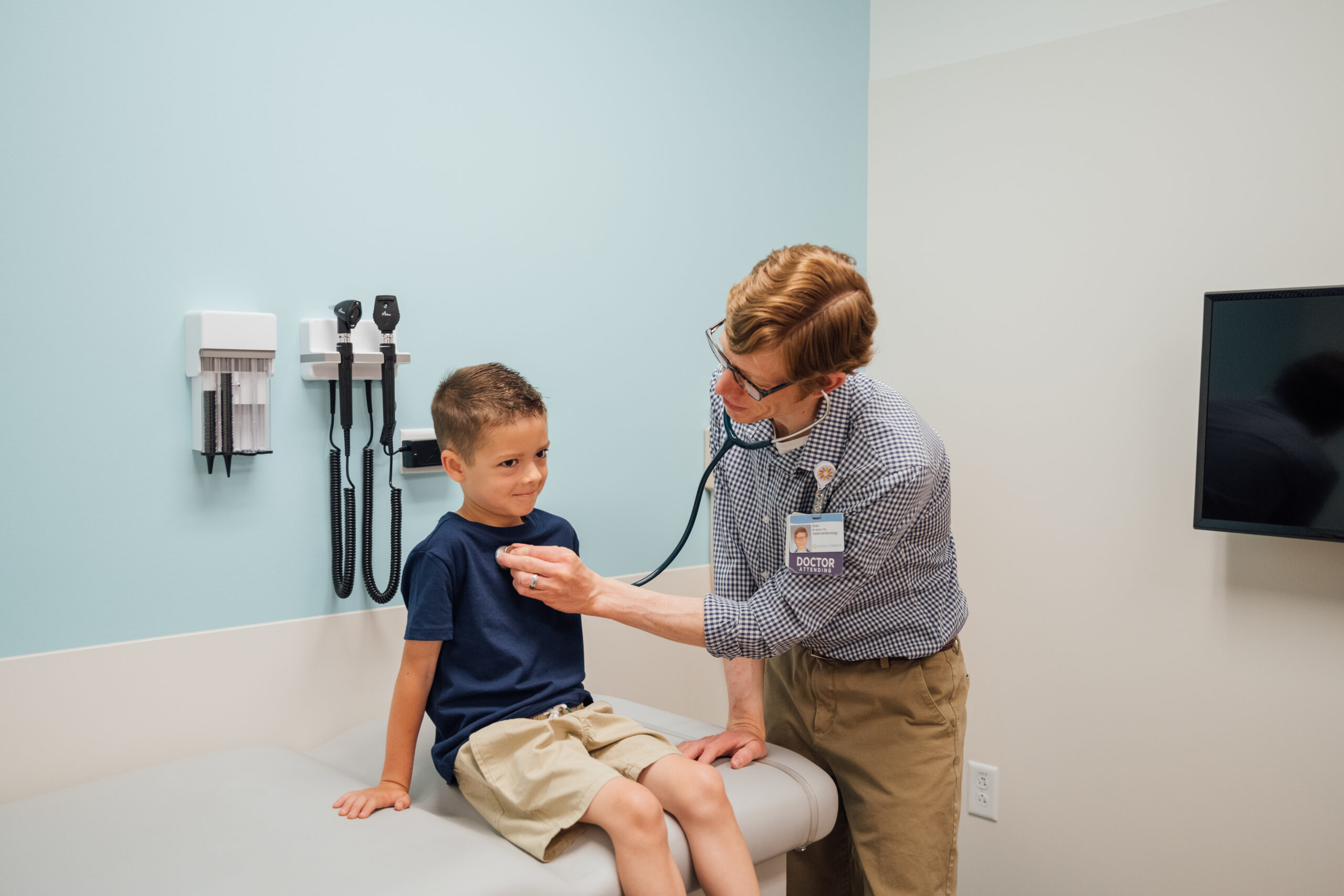 A pediatric gastroenterologist listens to a young boy's heart during an appointment.