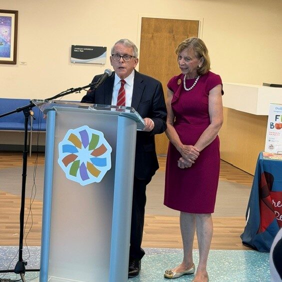Governor Mike DeWine speaks at podium with First Lady Fran DeWine standing next to him.