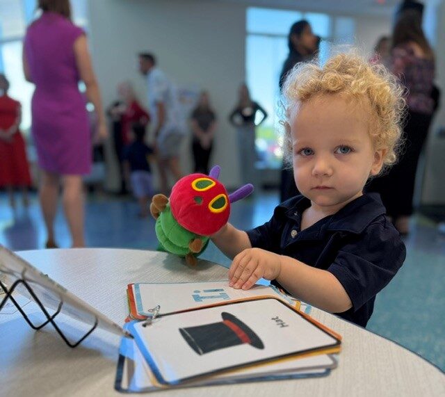 Toddler with short, curly hair and dark t-shirt holds a stuff animal caterpillar and looks through flashcards for kids.