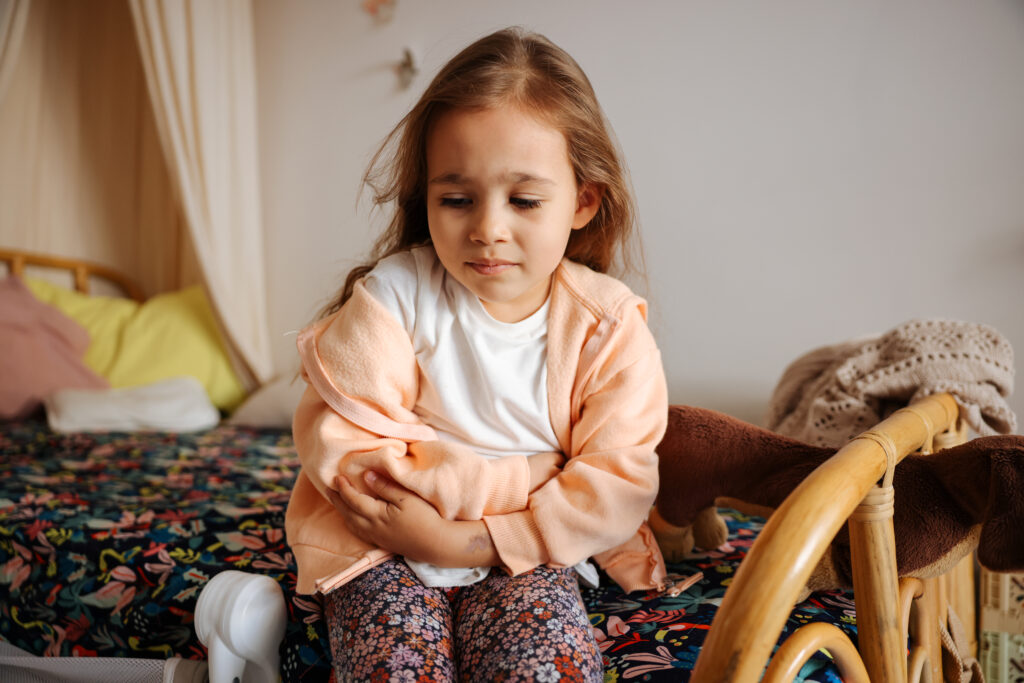 Young girl having stomach pain sitting on her bed at home.