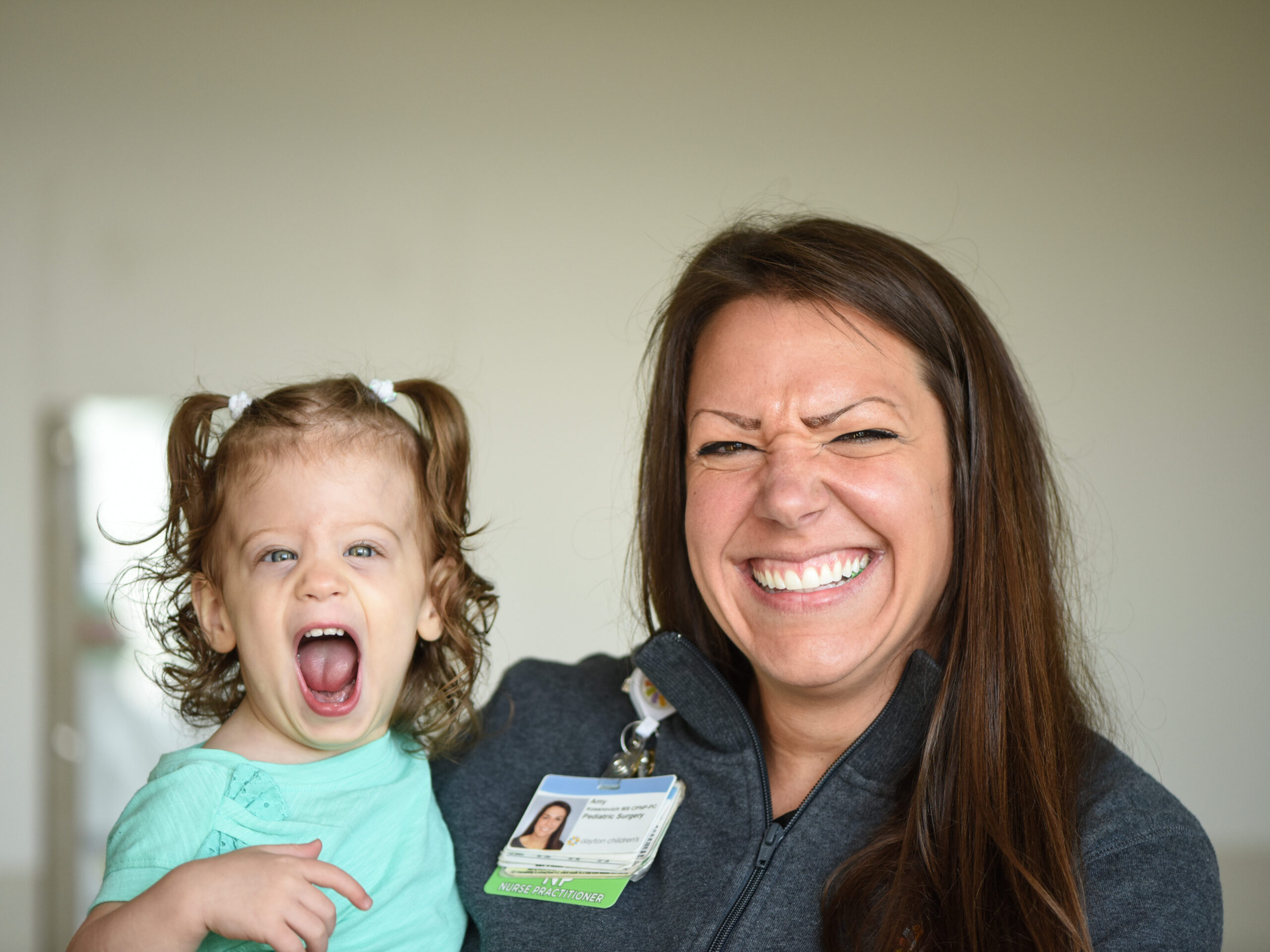 A smiling little girl laughing with her nurse and looking at the camera.