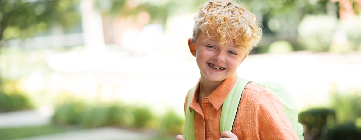 A young boy smiling while wearing a bright green backpack, feeling ready for back to school.