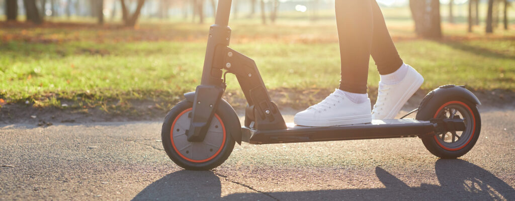Teen riding e-scooter on paved path.