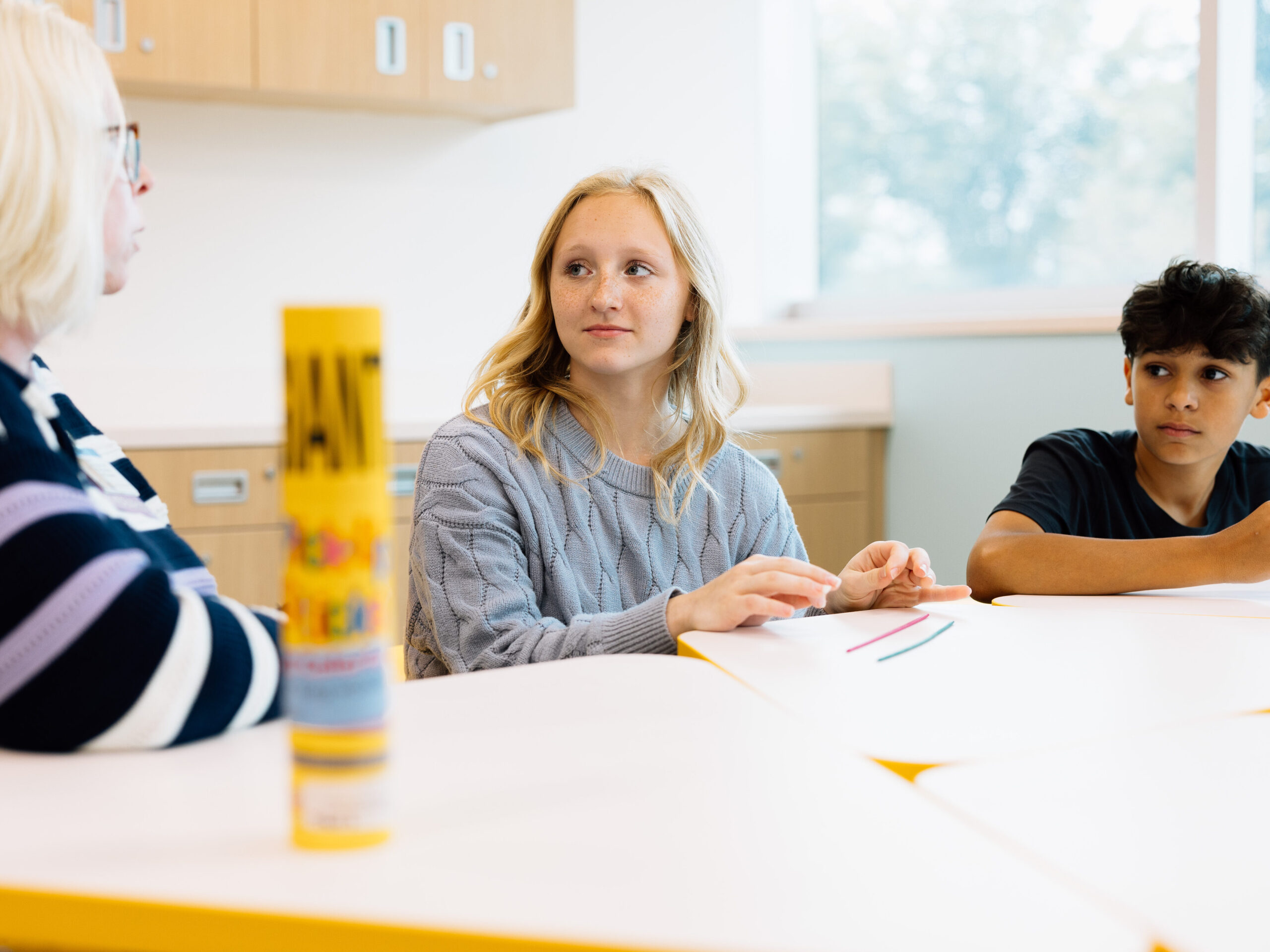Young teen girl and boy sit at table with mental health therapist during art therapy